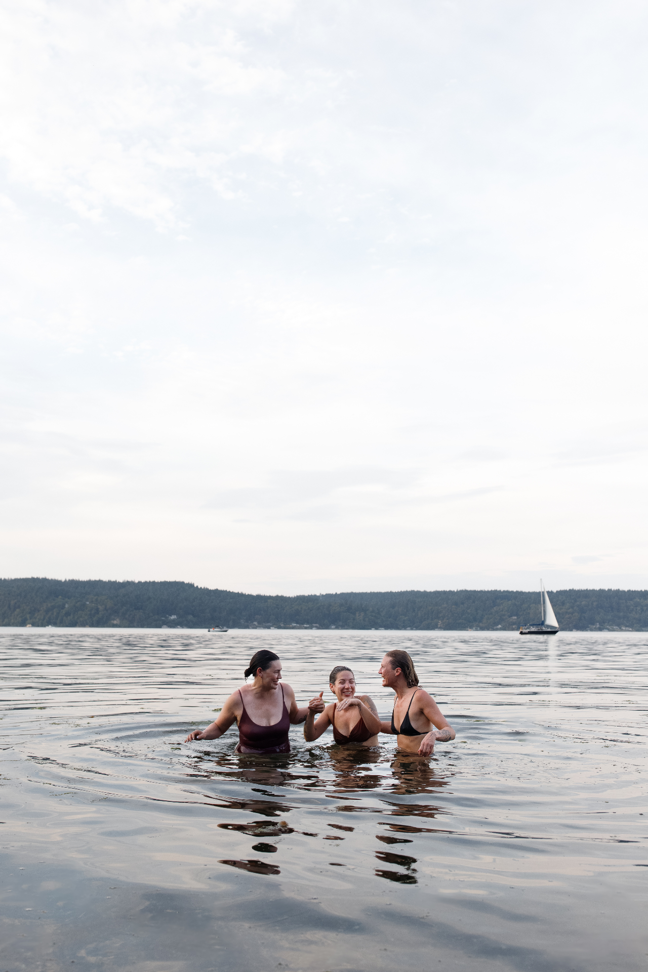 Three guests enjoying a cold plunge in the Puget Sound with a sailboat in the distance